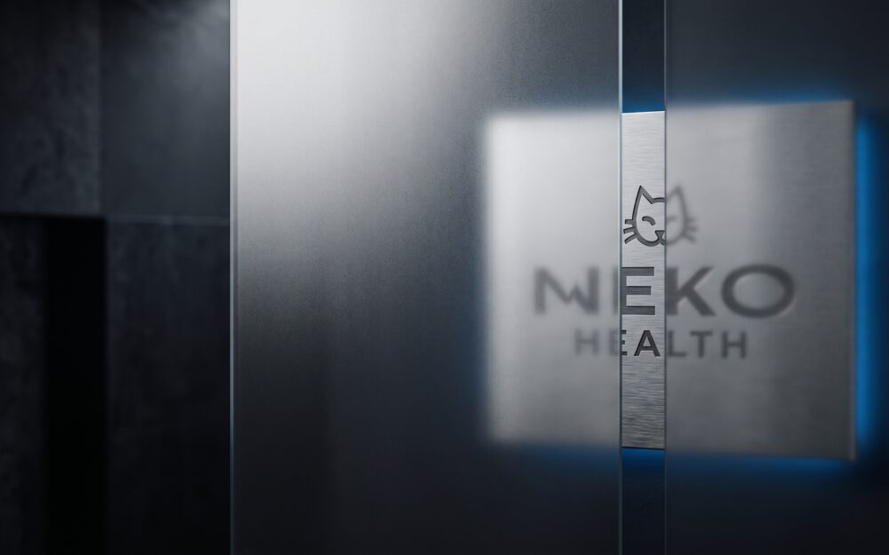 Neko Health logo on a brushed metal plate, partly behind frosted glass with one clear strip, lit by a thin blue edge